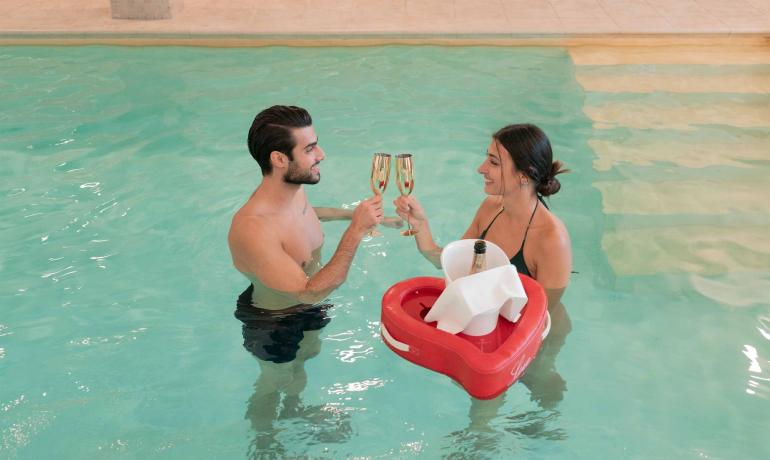 Paar stößt im Pool mit Gläsern und Champagner an.