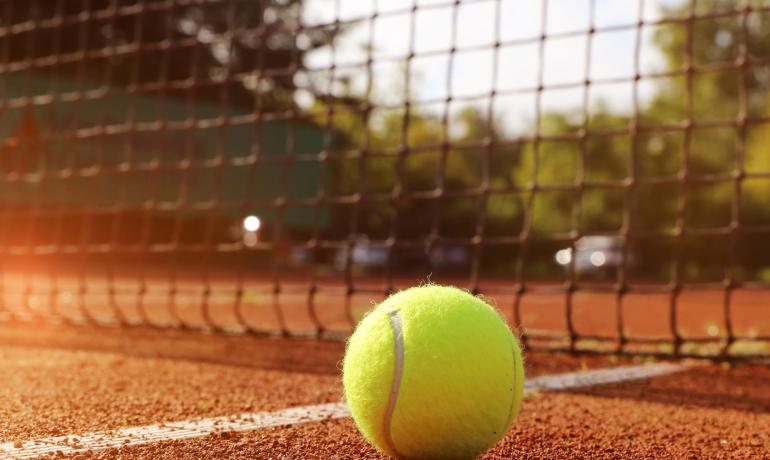 Tennis ball on clay court, near the net.